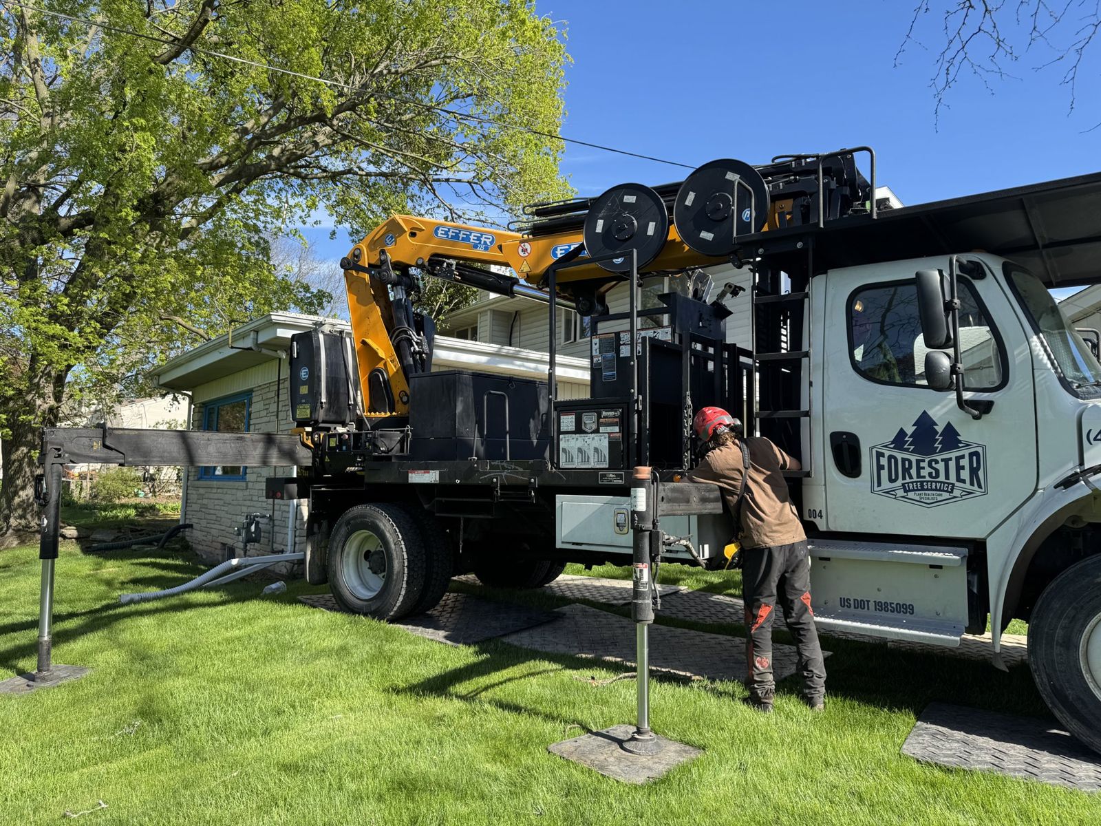 A Forester arborist in a helmet setting up a branded crane truck on a client's lawn